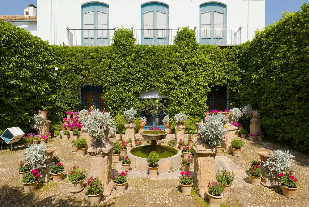 Patio con setos y macetas de flores del Palacio de Viana, con galería de ventanas al fondo